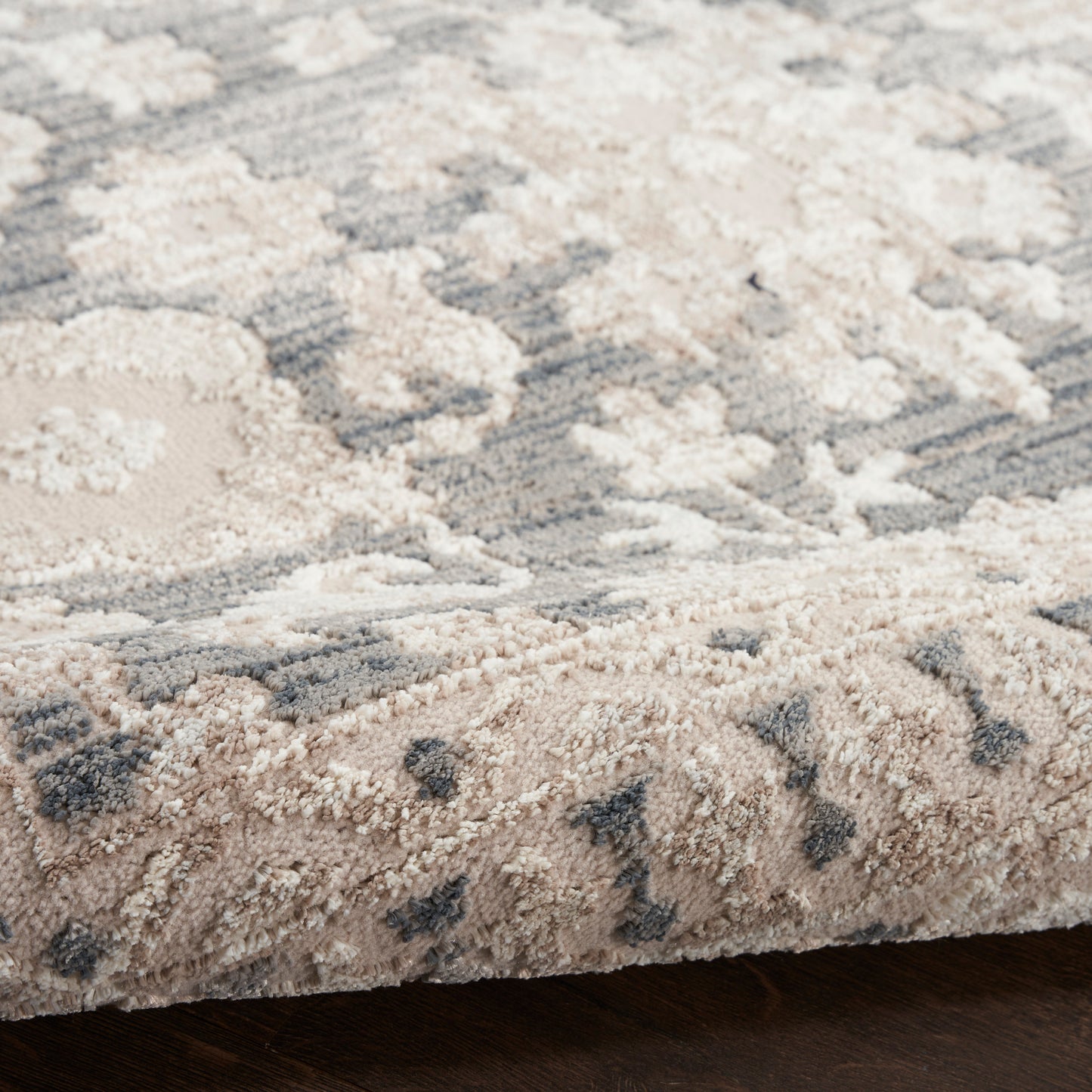 Soft high-pile rug in beige and gray with a subtle floral/medallion pattern; folded edge shows plush fibers.