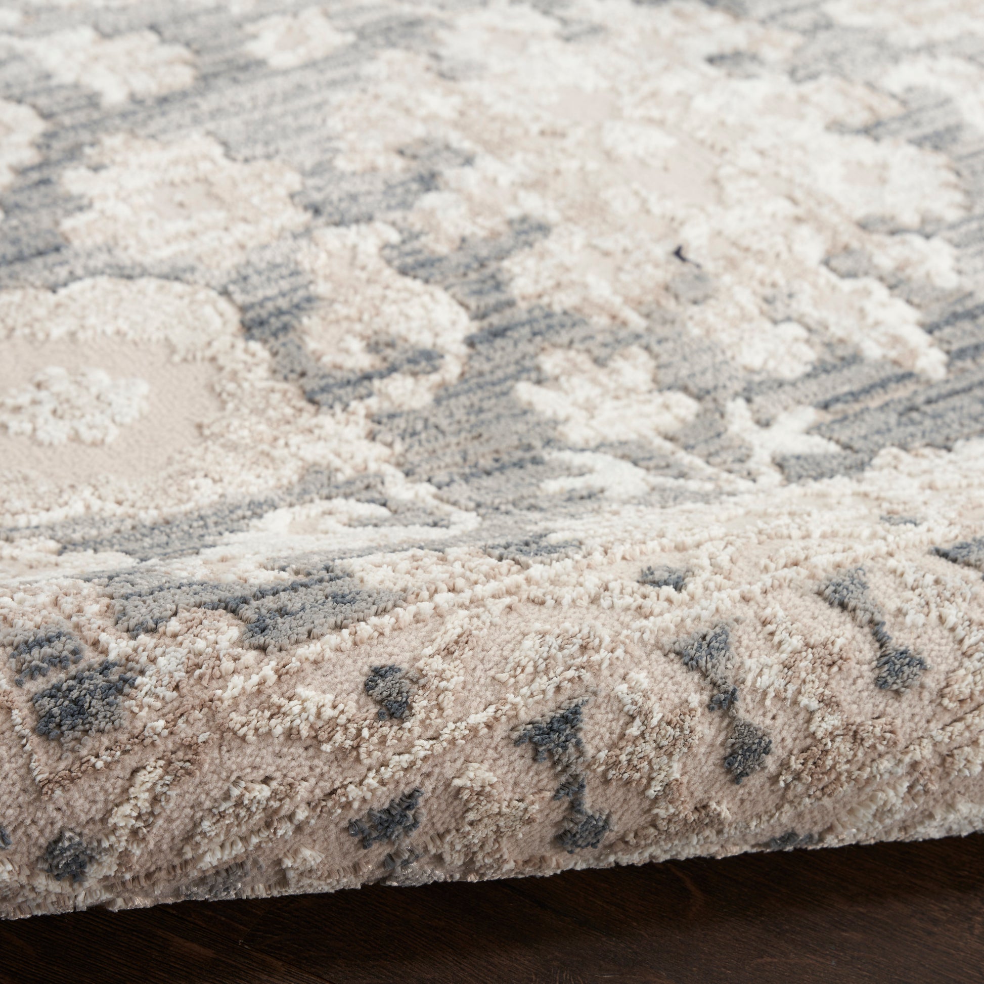 Soft high-pile rug in beige and gray with a subtle floral/medallion pattern; folded edge shows plush fibers.