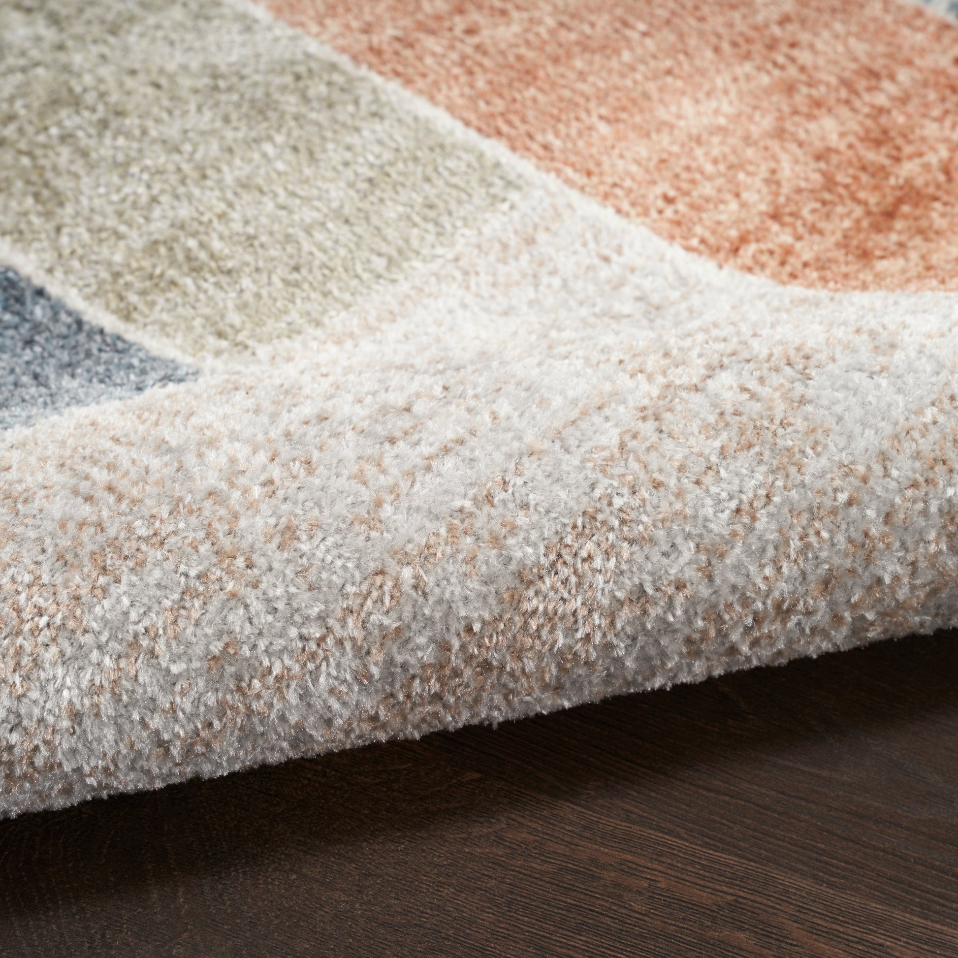 Close-up of a plush area rug with cream, beige, gray and peach color blocks on a dark wooden floor.
