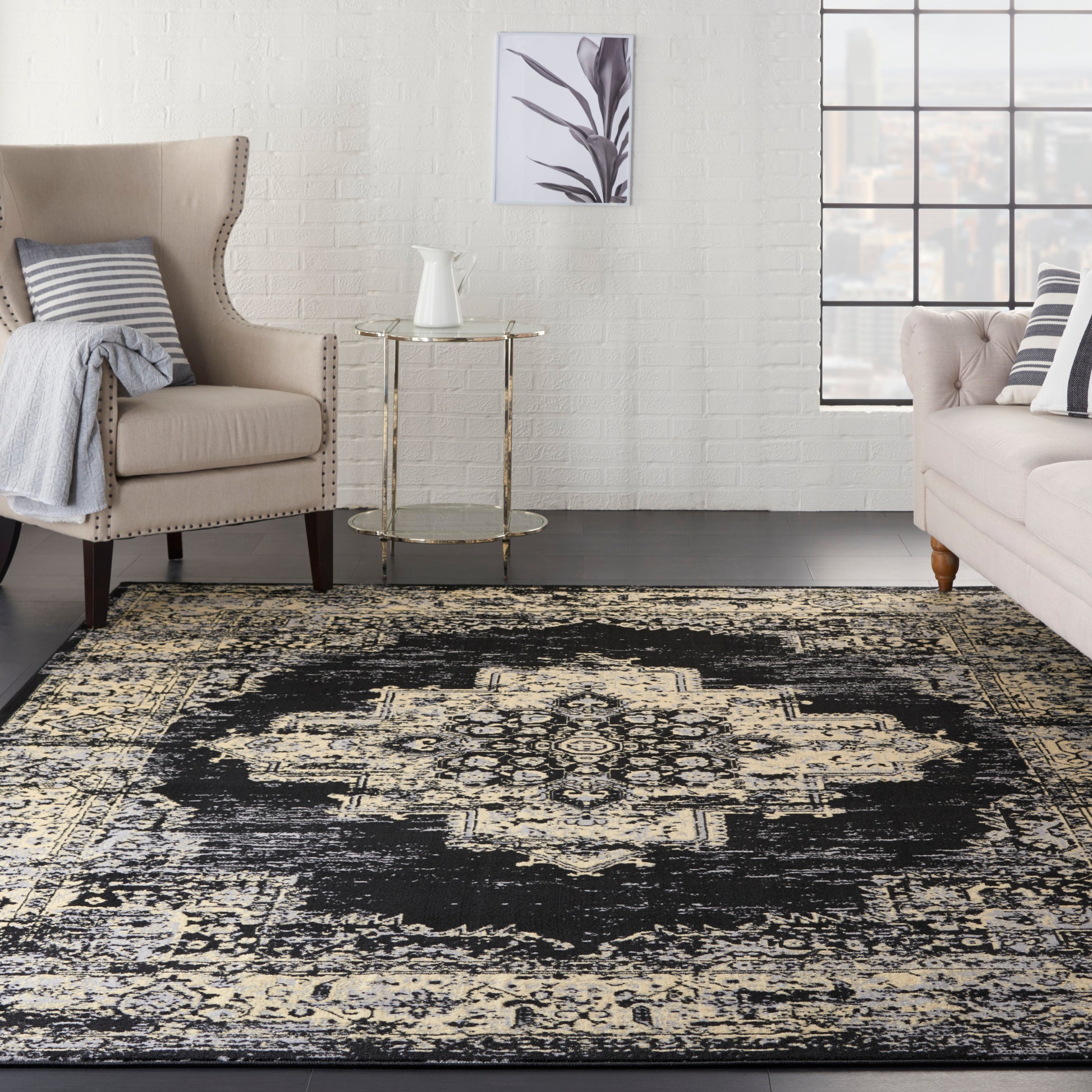 Black and ivory distressed oriental rug in a beige living room with tufted chairs, glass-top gold side table, and white brick wall.