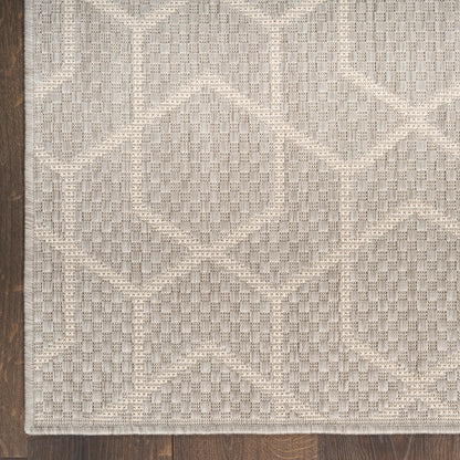 Beige textured area rug with checkerboard and diamond geometric pattern on dark wood floor.