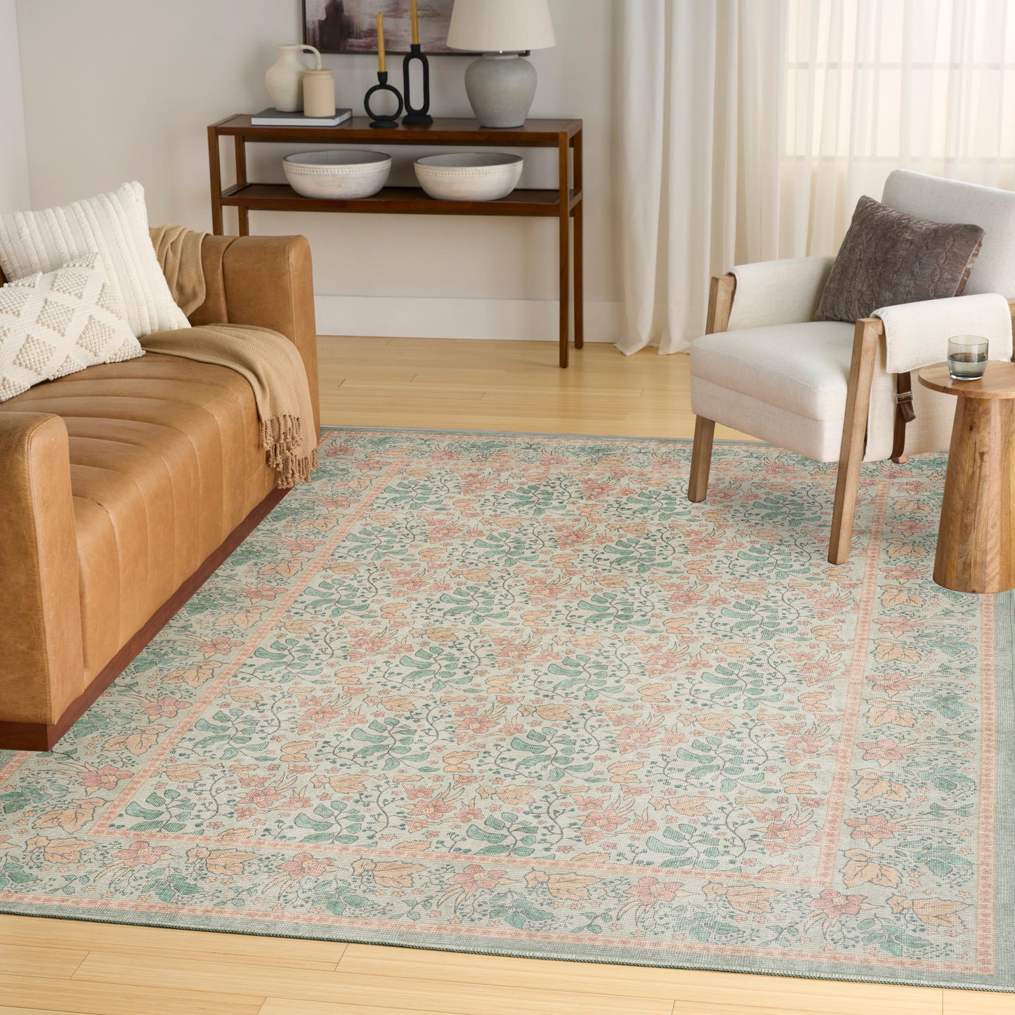 Living room with pastel teal and peach floral area rug, tan sofa, light gray armchair, wooden side table.