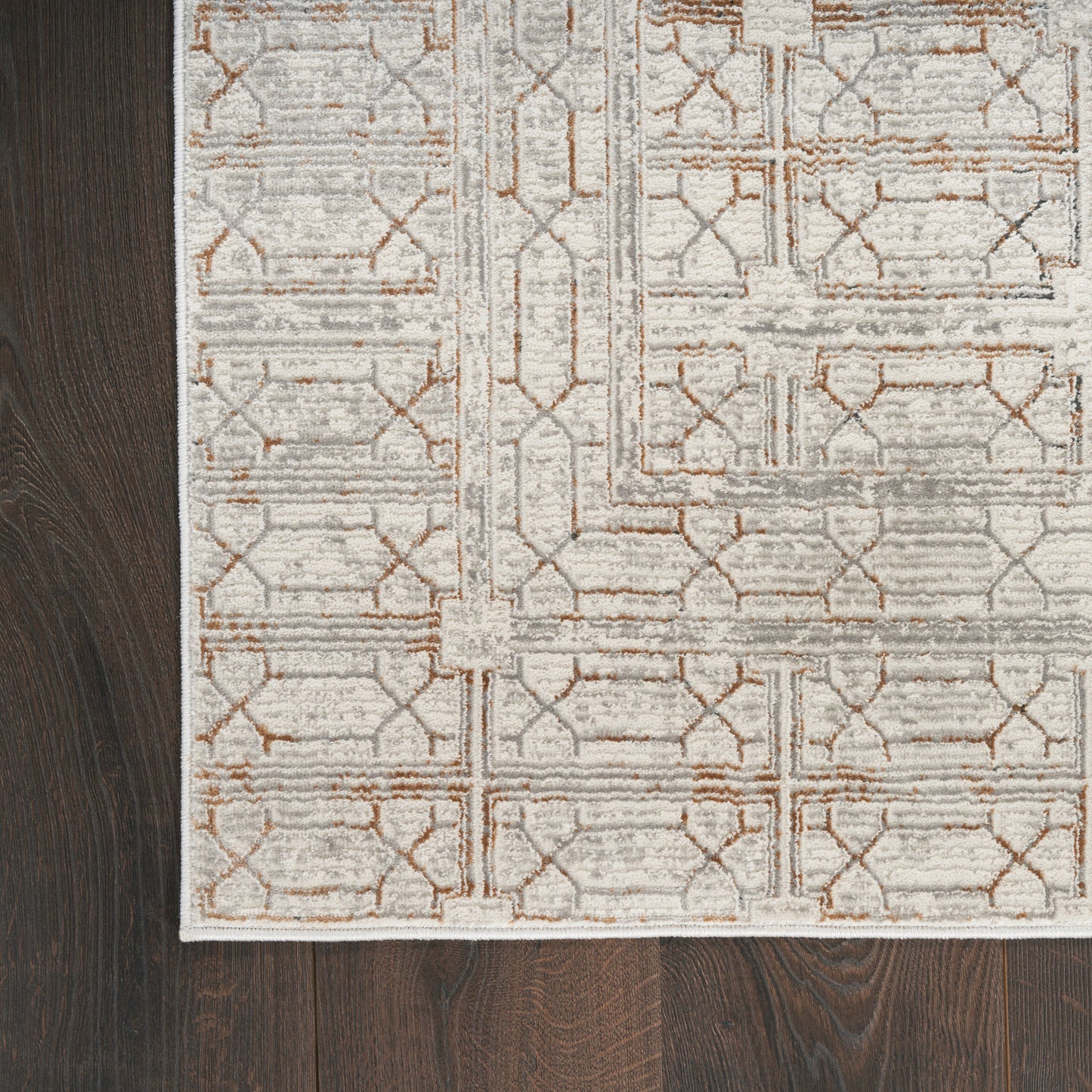 Soft ivory geometric area rug with tan lattice pattern and pale border on dark hardwood floor.