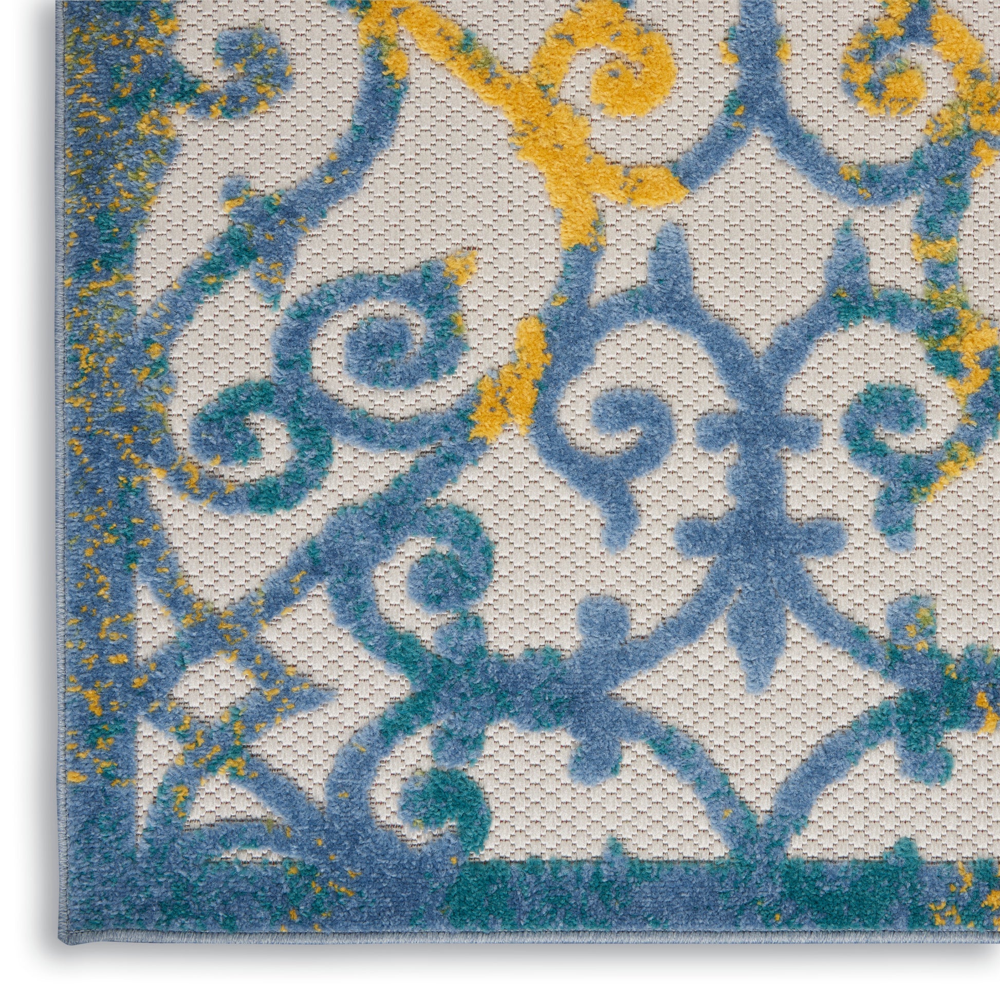Close-up of blue and turquoise ornamental scrollwork with yellow speckles on a textured cream rug.