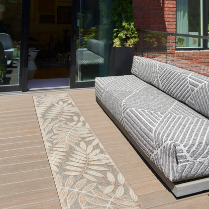 Outdoor lounge: grey patterned modular sofa on a wooden deck with a beige leaf-pattern rug beside sliding glass doors.