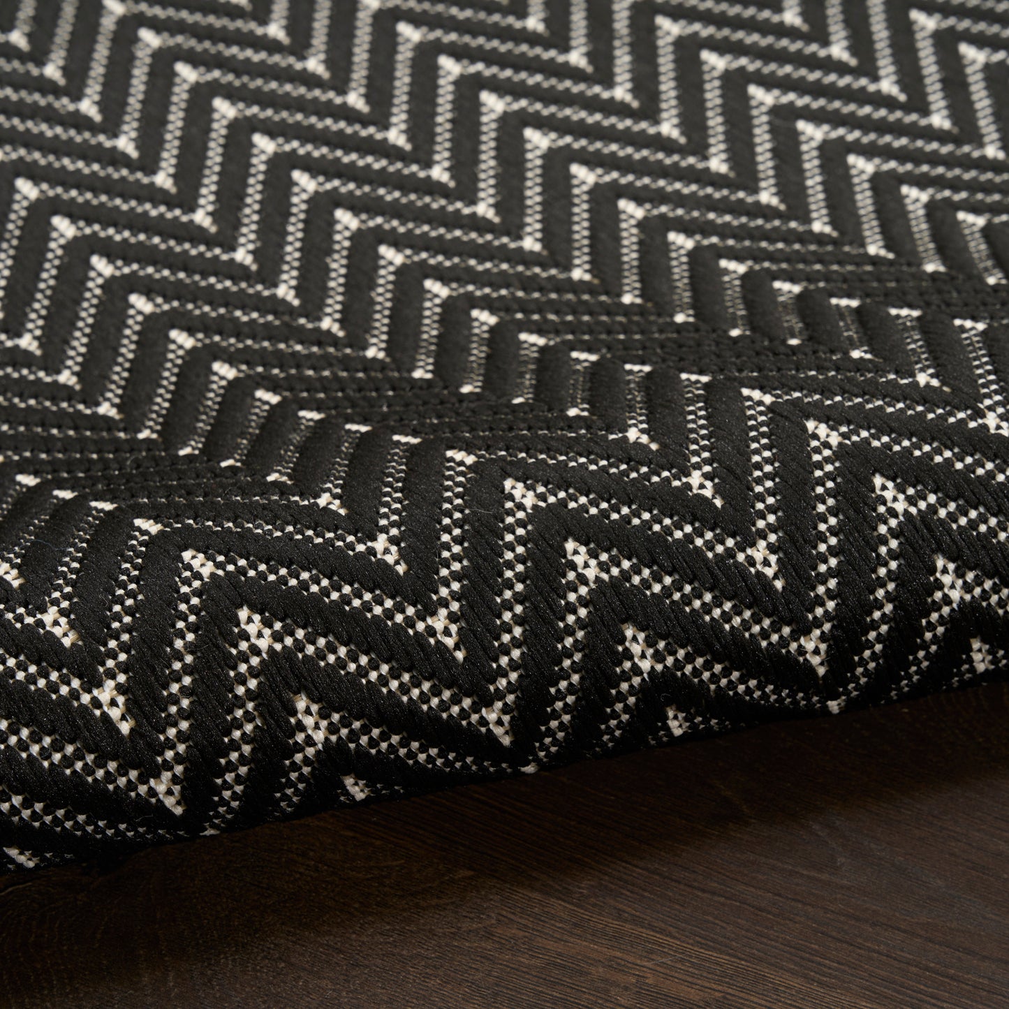 Close-up of black and white chevron zigzag woven rug fabric on dark wood floor