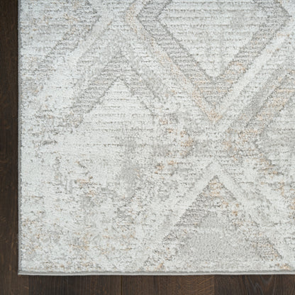 Light gray area rug with ivory geometric diamonds and chevrons on dark hardwood floor.