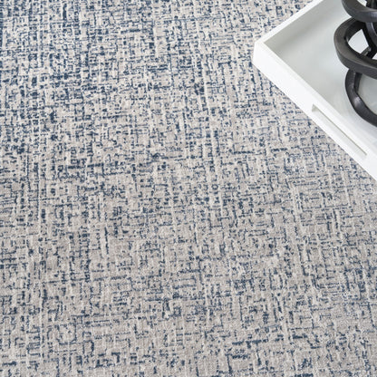 Blue and beige abstract patterned area rug with textured weave; corner shows white tray with black sculptural coil.