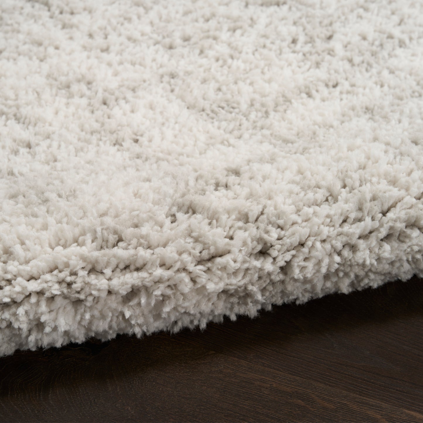 Cream shaggy rug with plush, fluffy pile on dark wood floor.
