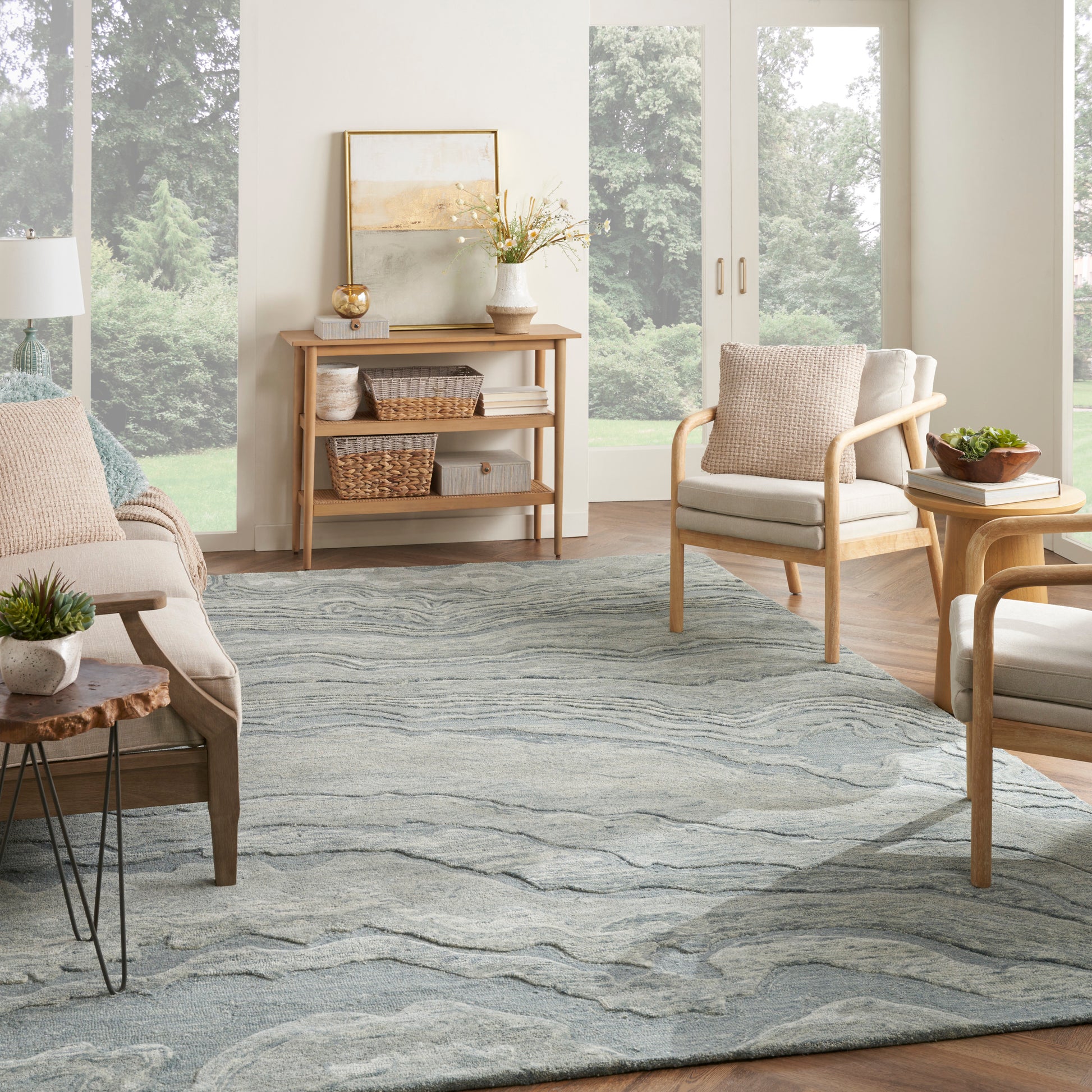 Bright living room with natural wood furniture, light upholstery, and a gray-blue wavy rug; wicker baskets on a console.