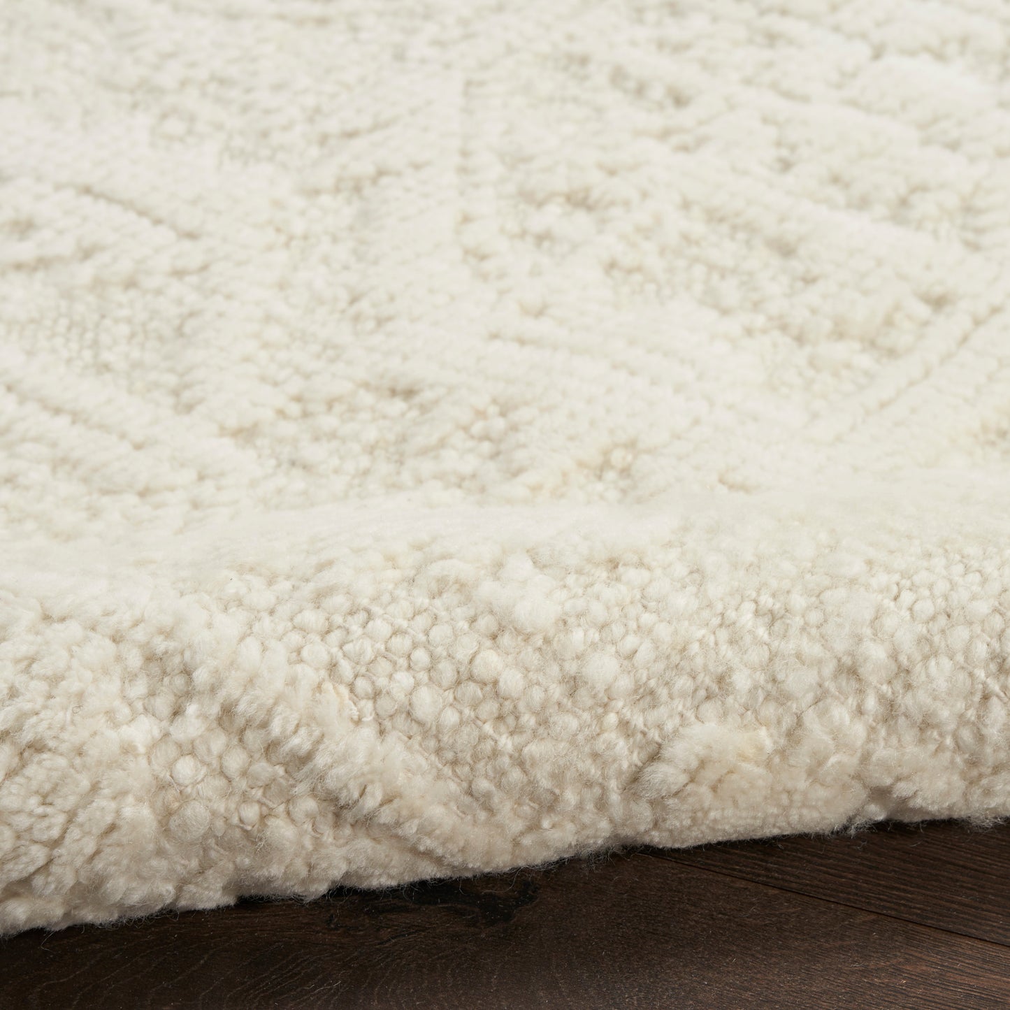 Cream boucle-pile shag rug with plush fibers on dark wooden floor.