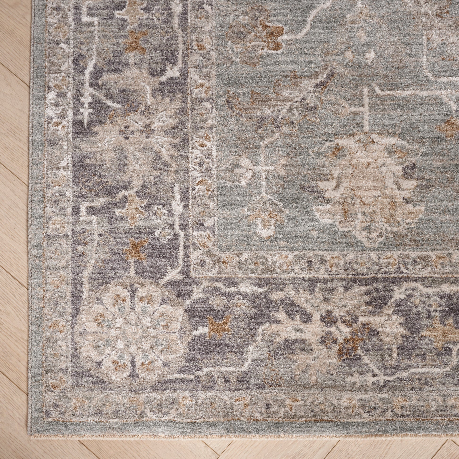 Blue-gray distressed oriental rug with beige floral border on light wood floor.