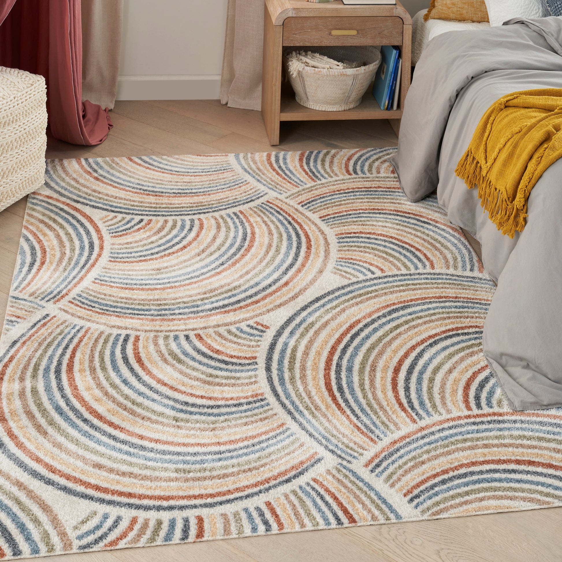 Rectangular tufted area rug with blue, orange and beige concentric arc patterns in a bedroom.