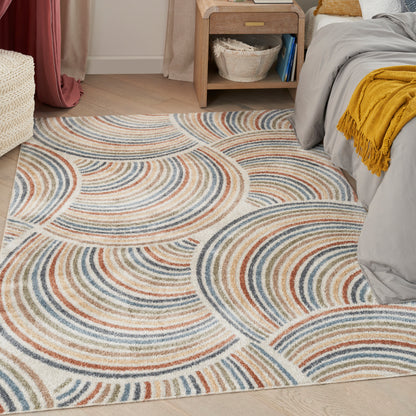 Rectangular tufted area rug with blue, orange and beige concentric arc patterns in a bedroom.