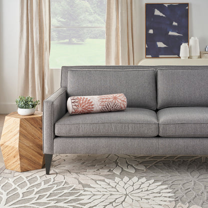 Gray fabric mid-century sofa with pink botanical bolster pillow, wooden side table, beige curtains, blue abstract wall art.