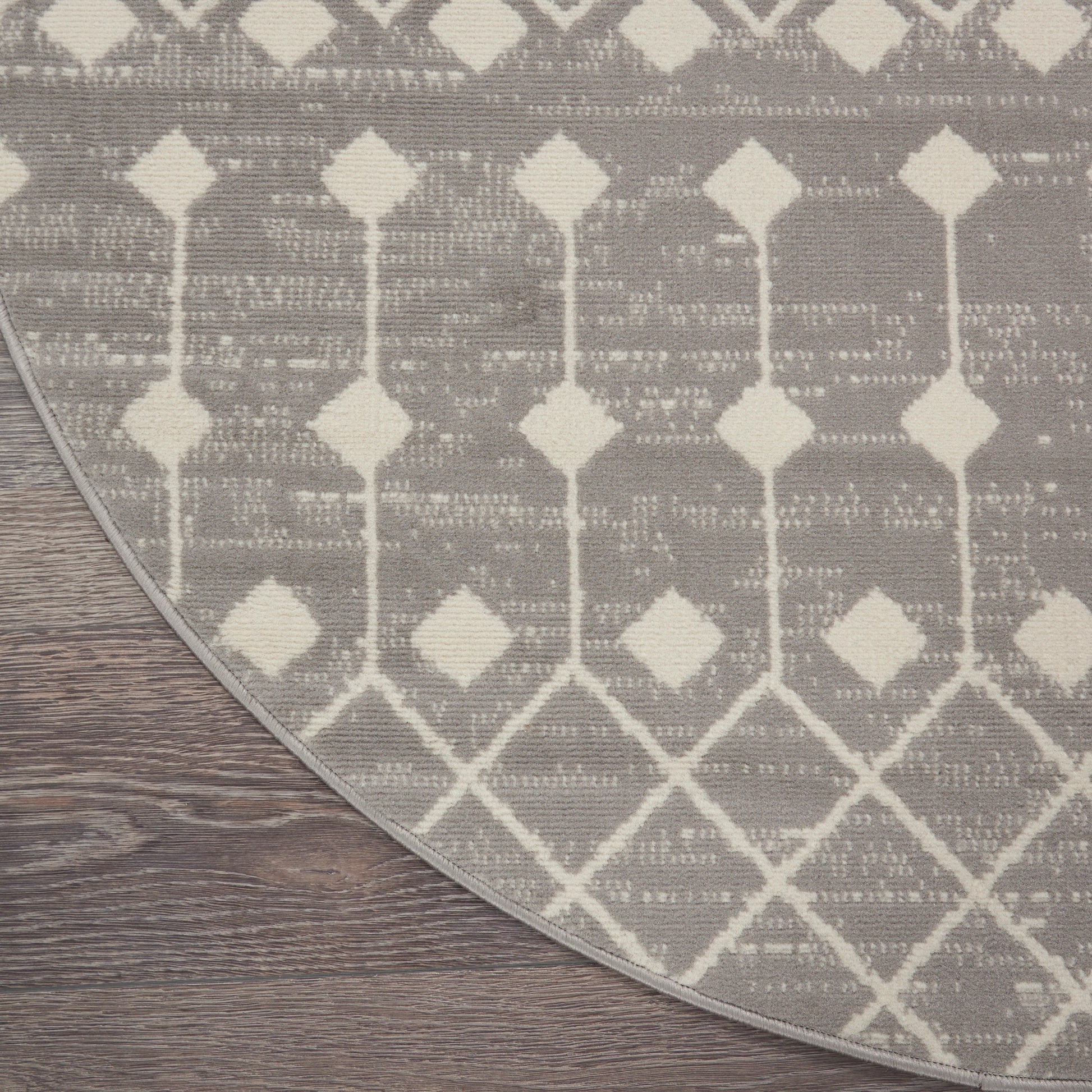 Round gray rug with white geometric diamond pattern on dark wood floor.
