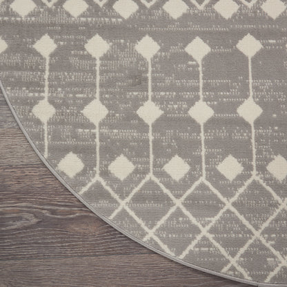 Round gray rug with white geometric diamond pattern on dark wood floor.