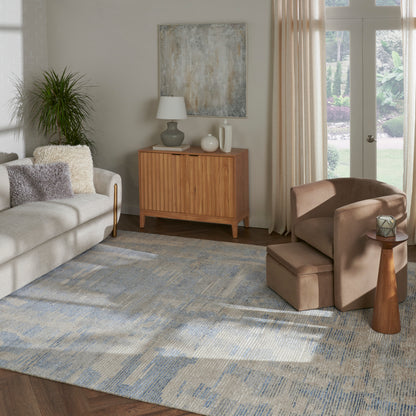 Living room with beige sofa, mid-century wooden sideboard, blue-gray rug, brown armchair and ottoman, plant, French doors.