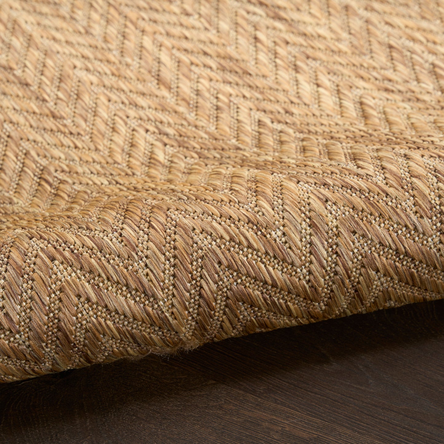 Natural jute rug with zigzag chevron weave in tan and beige, close-up edge resting on dark wood floor