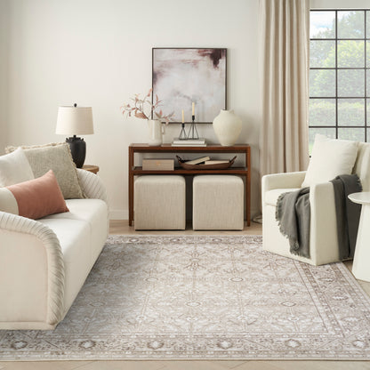 Neutral living room featuring cream sofa, pale pink pillows, beige armchair, wooden console, two ottomans, and a patterned rug.