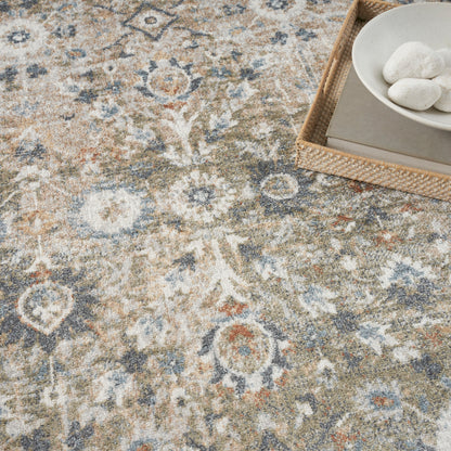 Distressed vintage-style floral rug in beige, blue and ivory; wicker tray with a book and white stones in corner.