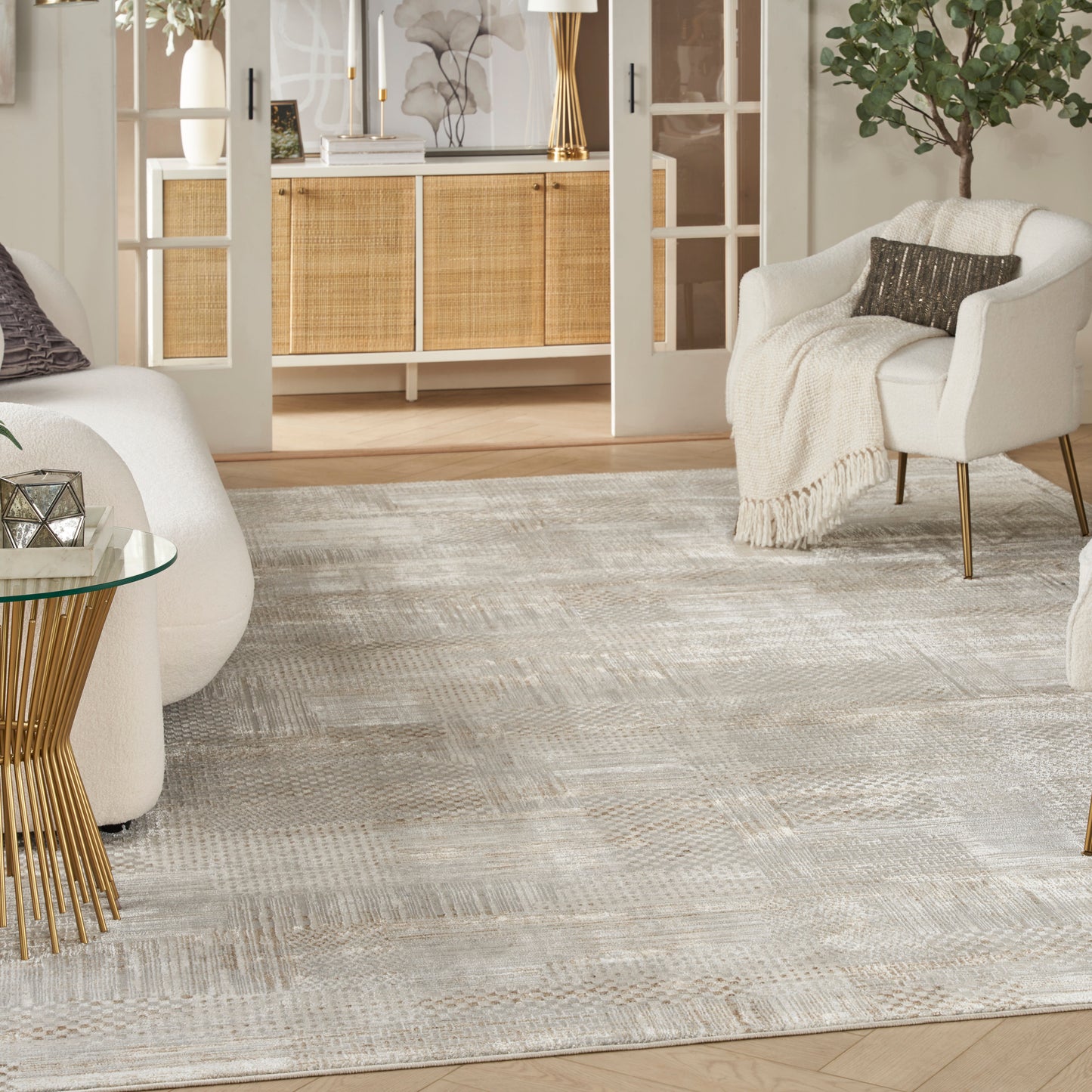 Neutral living room with white armchairs, beige throw, glass table with gold legs, woven rug & a rattan cabinet.
