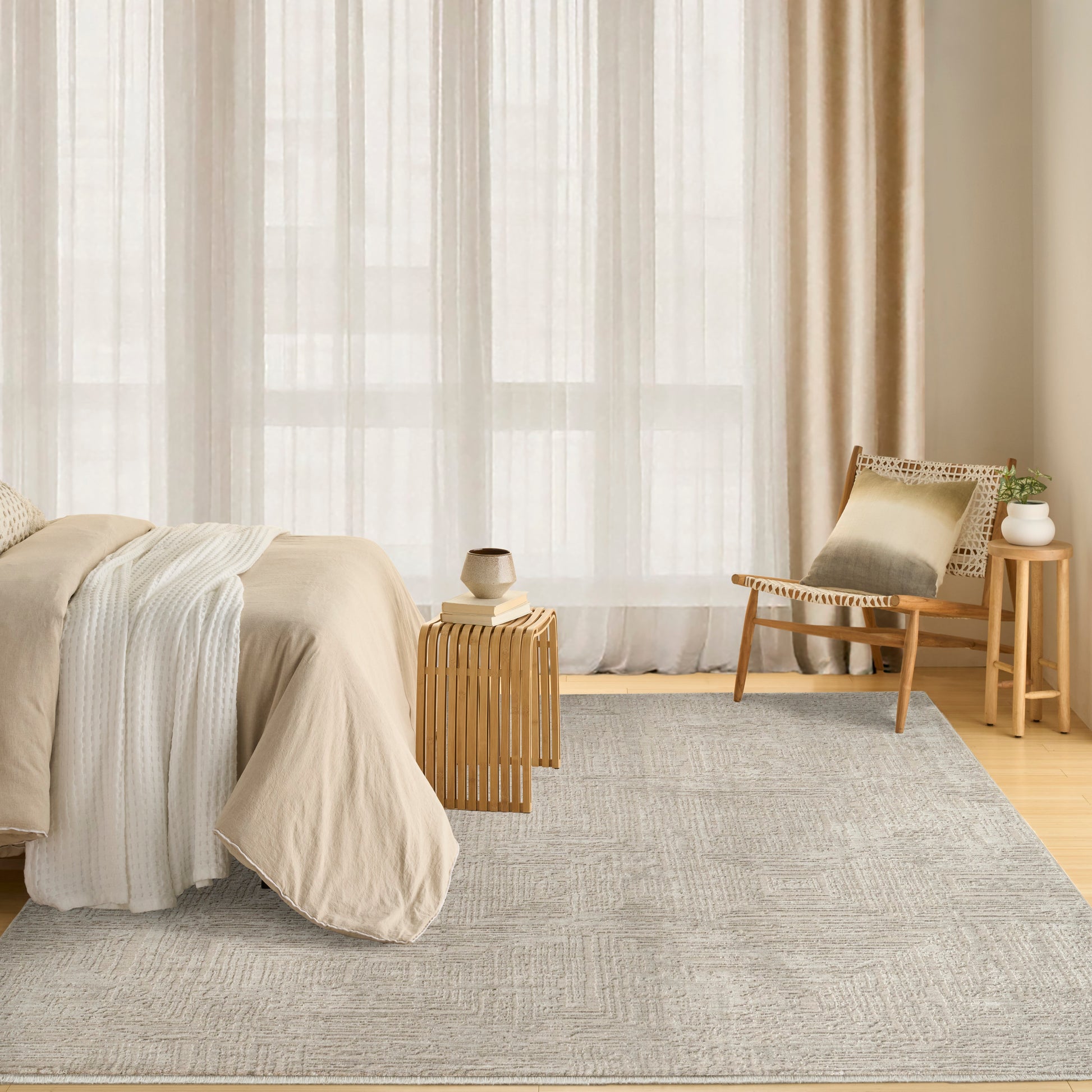 Neutral bedroom with beige bedspread, white throw, light wood furniture, woven chair, small wooden tables, and a gray rug.