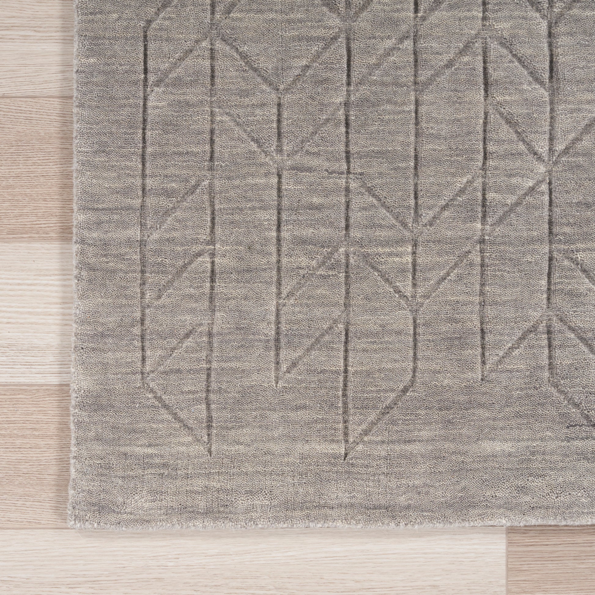 Gray geometric area rug with linear chevron pattern and soft woven texture on light wood floor.