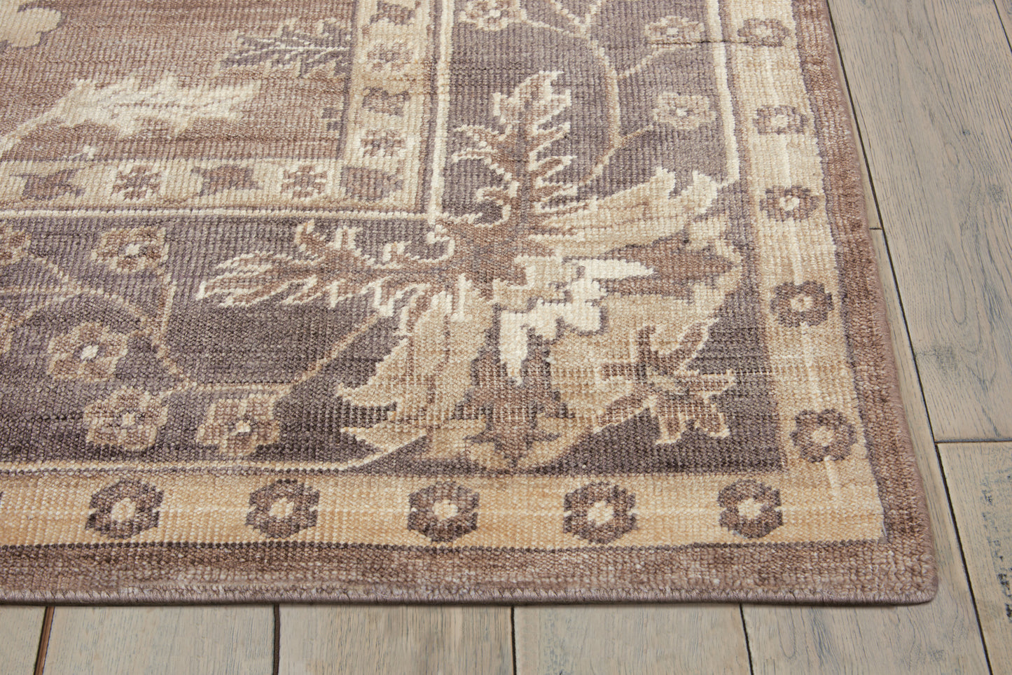 Rectangular oriental-style area rug in tan, beige and brown with floral border on wood floor.