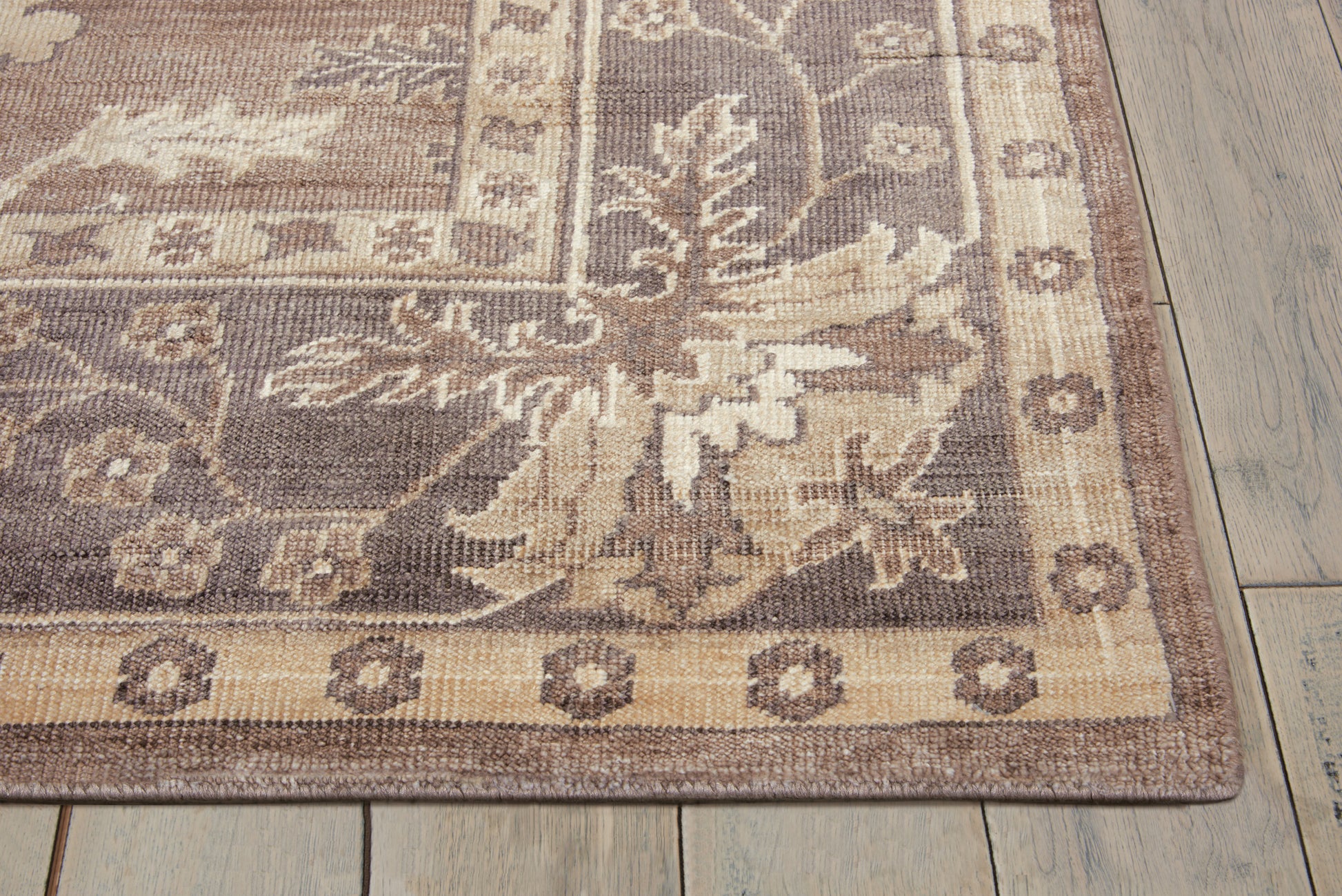 Rectangular oriental-style area rug in tan, beige and brown with floral border on wood floor.