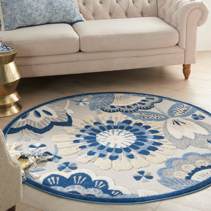 Round woven rug in blue and cream floral pattern on a light wood floor beside a beige tufted sofa.