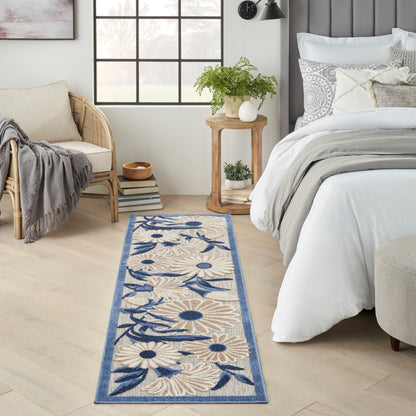 Woven blue floral runner rug with beige background along a light wood floor beside a bed with white linens and rattan chair.