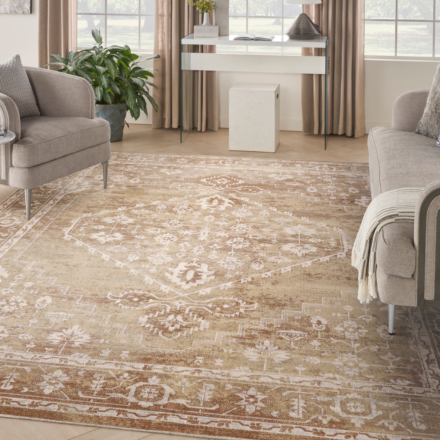 Neutral living room with beige ornate area rug, gray upholstered chairs, light wood floors, and a glass desk by windows.