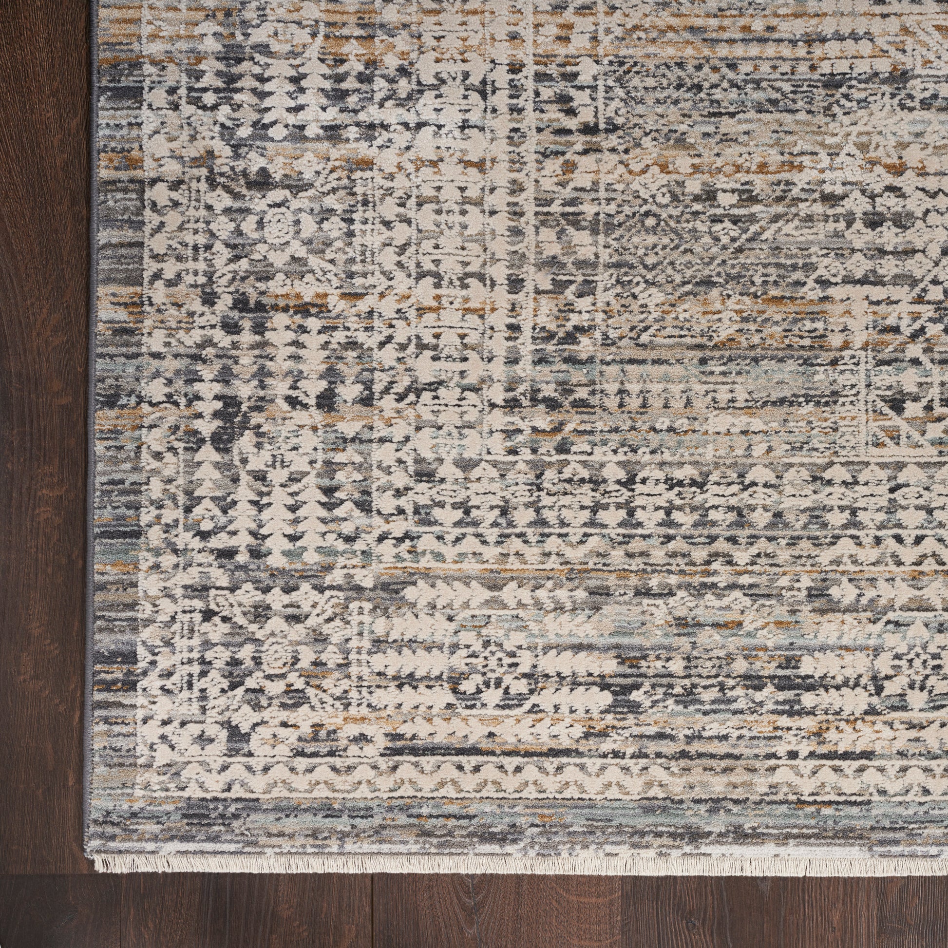 Distressed blue-gray oriental rug with ivory, tan and gold accents, fringed border on dark wood floor.