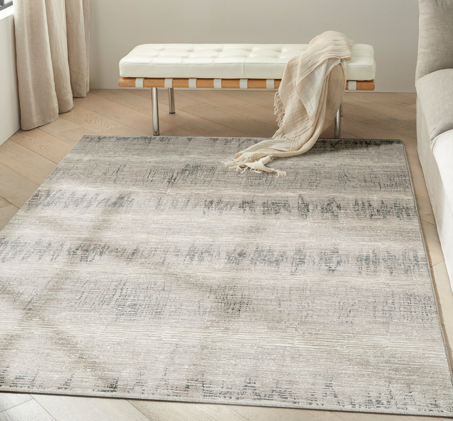 Large neutral area rug with a distressed gray-beige gradient pattern in a modern living room beside a white tufted bench.