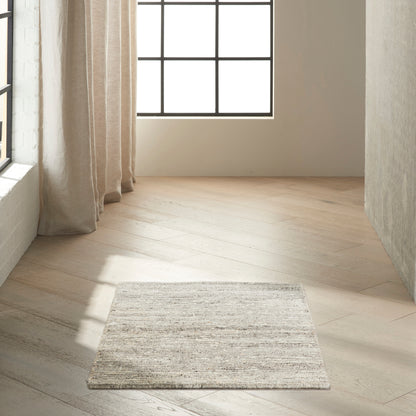 Neutral woven rectangular area rug in light gray-beige tones placed on light wood floor by a window with beige curtains.
