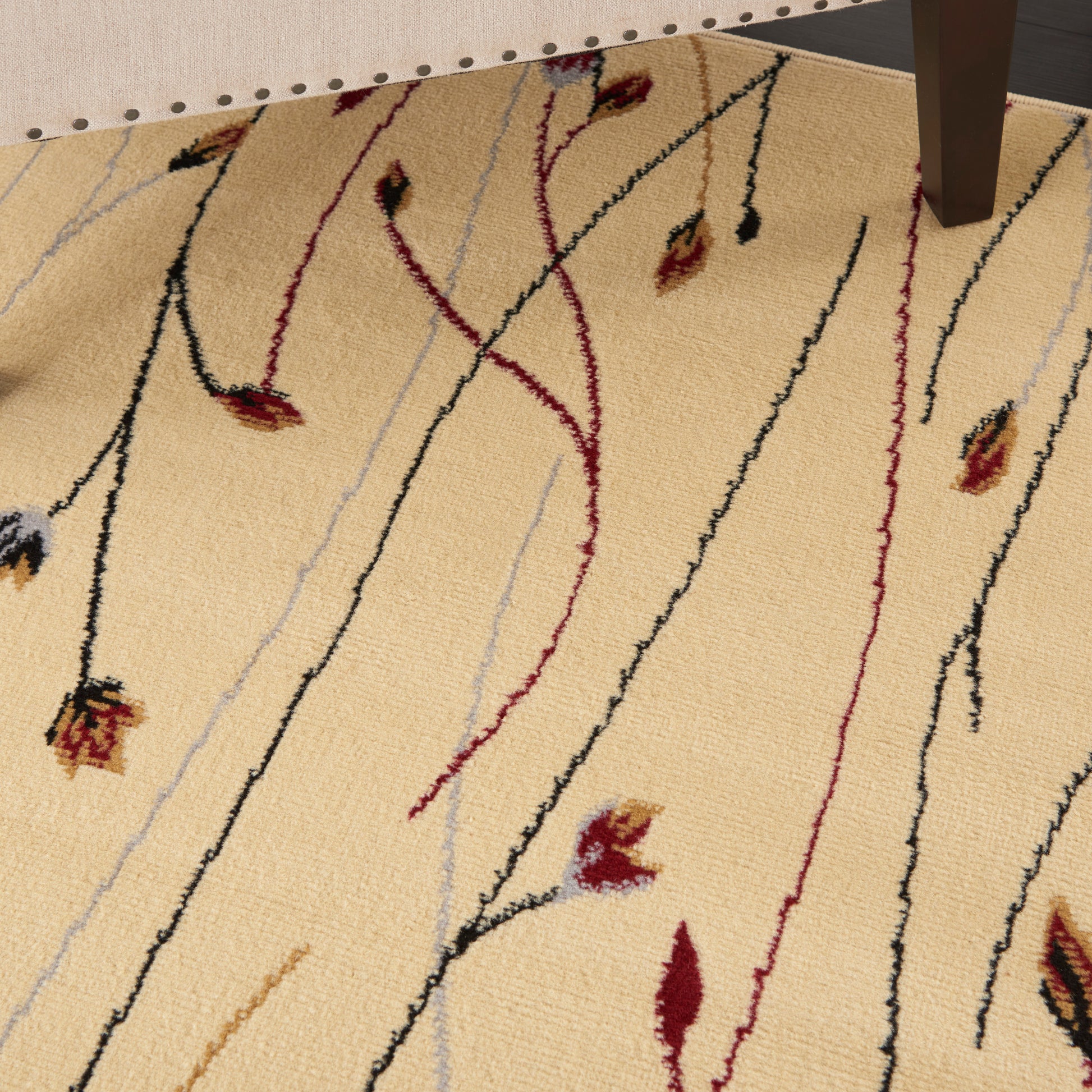 Beige rug with elongated vine-like black, red, and gray lines and small leaf buds; soft textured pile.