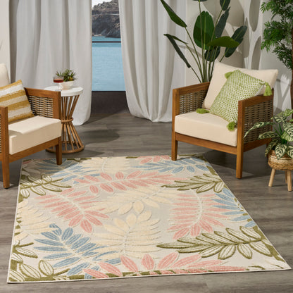 Rectangular rug with pastel pink, blue, and olive-green leaves on light beige, in a sunlit seating nook with wooden chairs.