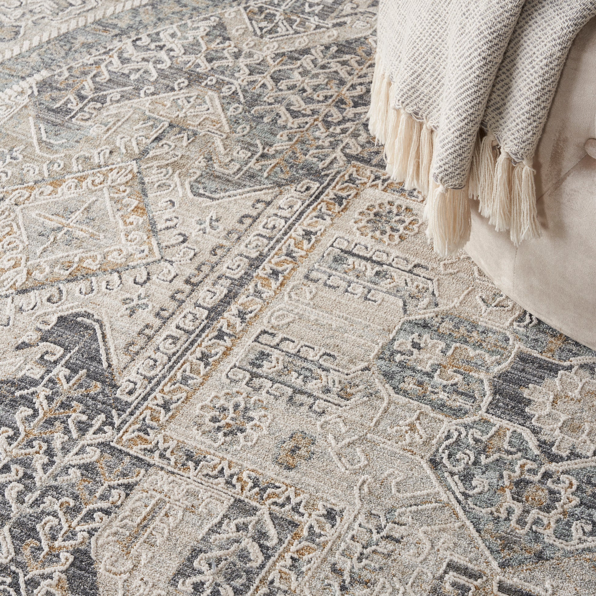 Woven geometric round area rug in ivory, gray & blue with fringe, paired with a beige sofa & cream tassel throw.