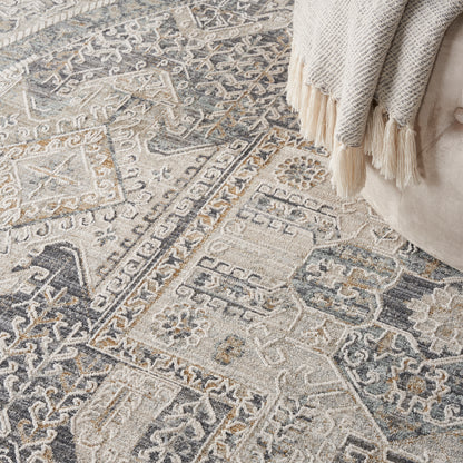 Woven geometric round area rug in ivory, gray & blue with fringe, paired with a beige sofa & cream tassel throw.