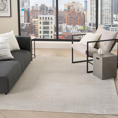 Modern living room with gray sofa, beige rug, metal-framed chair, end table and vase, city view through windows.