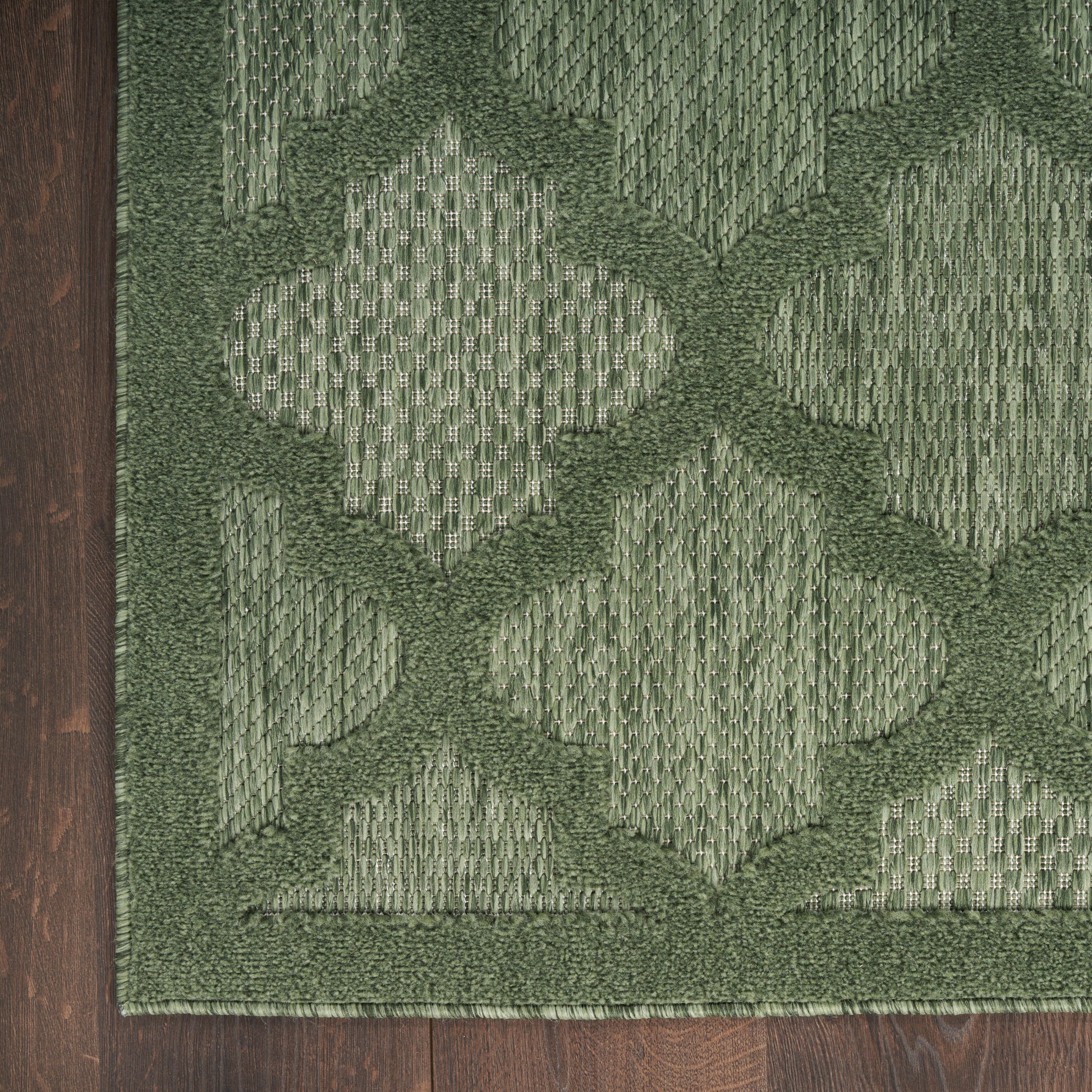 Green geometric patterned rug on dark wood floor; tufted diamond motif in olive and moss tones, rectangular area rug.