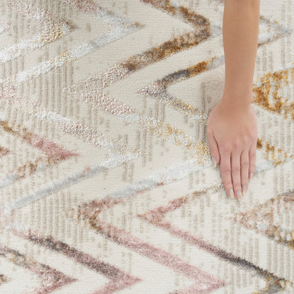 Close-up of a hand on a plush geometric zigzag rug in beige, cream, pink and brown tones.
