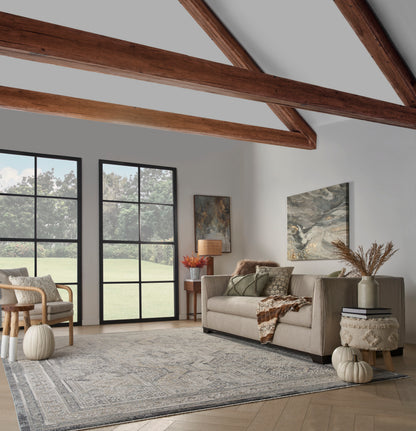 Cozy living room with beige sofa, wood-beam ceiling, large black-framed glass doors, patterned rug, pumpkins & autumn decor.
