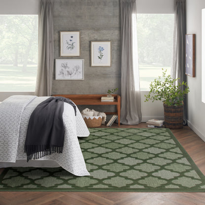 Bedroom with green geometric rug, white quilt bed, grey curtains, botanical art, wooden bench, basket and plant.