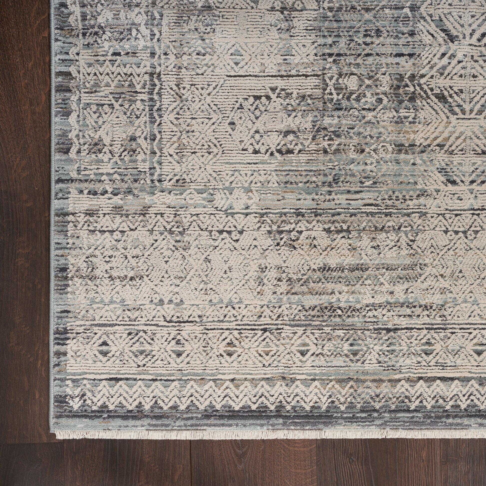 Distressed blue-gray oriental-inspired rug with ivory geometric motifs & fringe on dark wood floor.