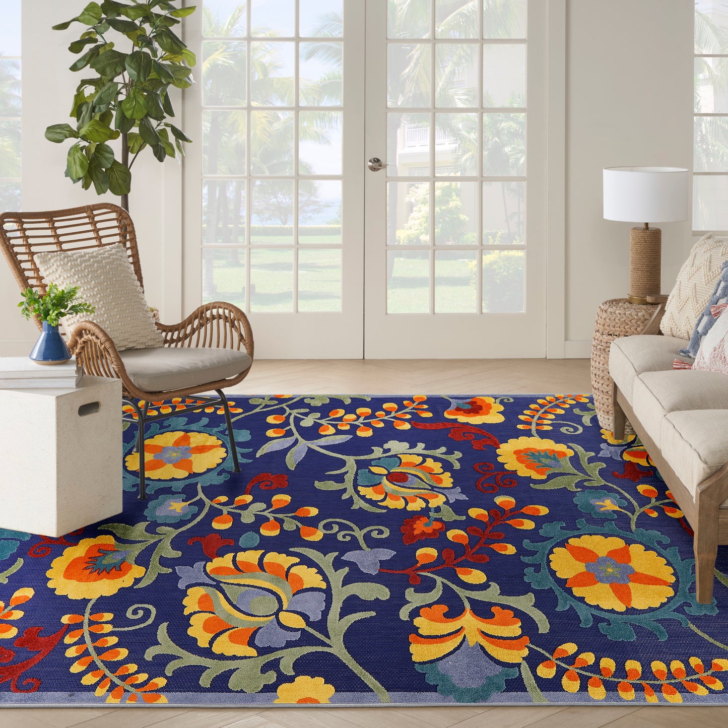Vibrant navy floral area rug with yellow, orange and red blooms and green leaves in a bright living room with wicker chair.