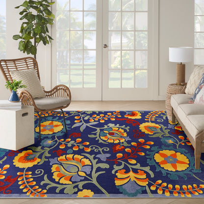 Vibrant navy floral area rug with yellow, orange and red blooms and green leaves in a bright living room with wicker chair.