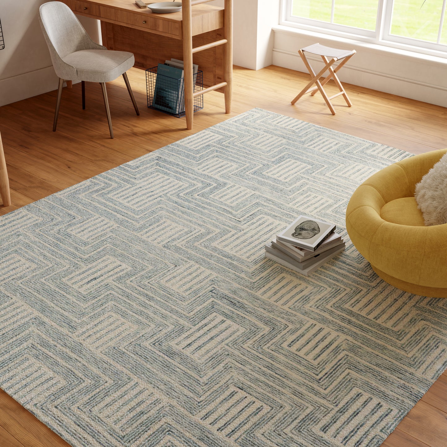 Light blue geometric area rug on warm wood floor in a bright living room with a yellow round chair and desk.