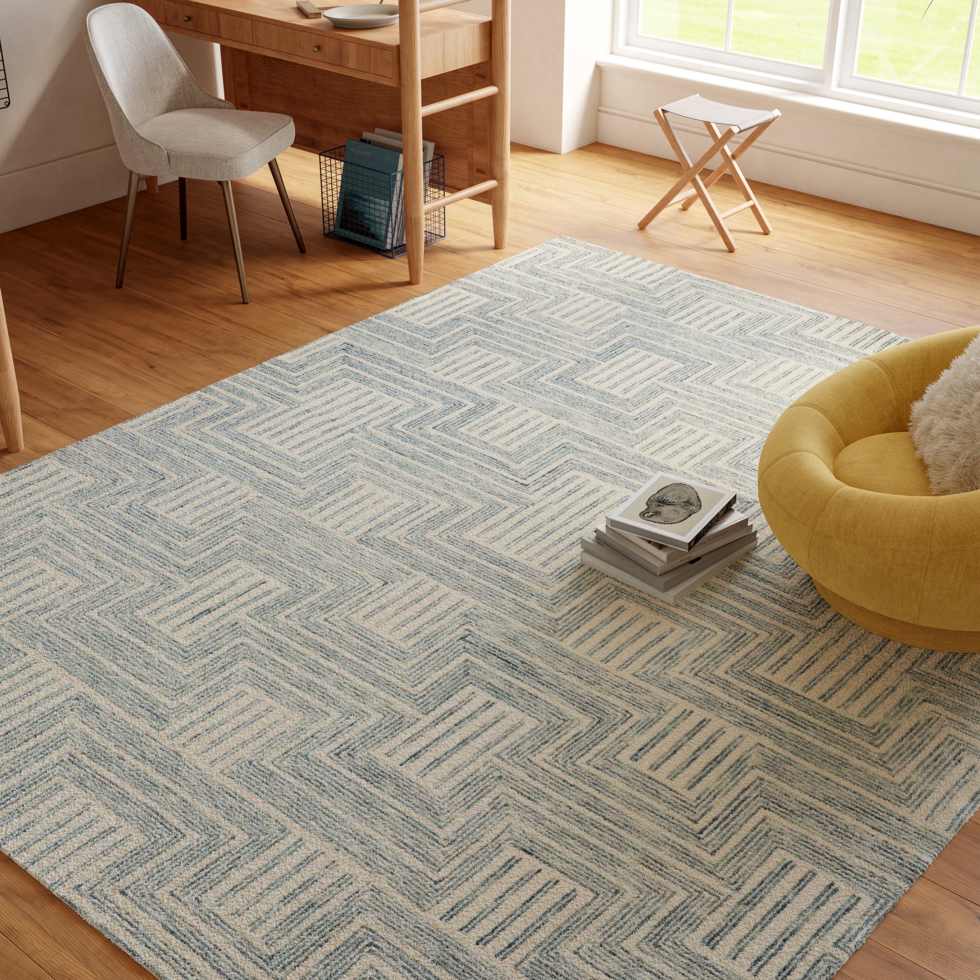 Light blue geometric area rug on warm wood floor in a bright living room with a yellow round chair and desk.